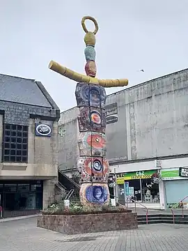 Abstract sculpture called the "earth goddess", five roundels made of ceramic carelessly splashed with orange, red, blue and yellow paint, with two yellow ceramic tubes like arms and three small roundels and a halo as a kind of "handle" for a kind of "skewer"