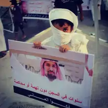 A young boy holds up a sign that has a photograph of Abdulla Majed Al Noaimi raising another board in one of his Human Rights protests.