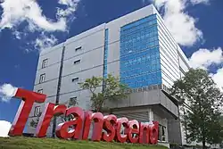 A view looking upward at a gray office building, with the Transcend logo in the grass in front