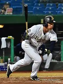 A man on a Baseball field in a Orix Buffaloes Uniform wearing a batting helmet starting a run from the batter's box.