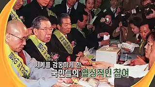 People sitting around a table, surrounded by reporters and photographers