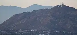 A mountain with a large painted M and several telecommunications towers on top