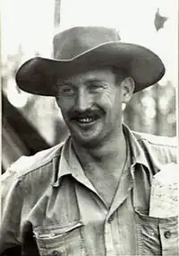 Informal portrait of grinning moustachioed man in wide-brimmed hat and military uniform