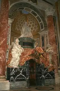 A large memorial set in a niche. The marble figure of a kneeling pope is surrounded by allegoric marble figures, and sculptured drapery surfaced with patterned red stone.