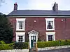 A brick house with four sash windows and a green front door.