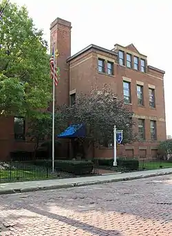 three story brown brick early 20th century school building with chimney and trees