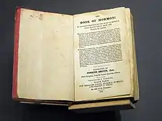 A photograph of the 1841 First European (London) edition of the Book of Mormon. It is open to its title page. The edges of the page are colored red.