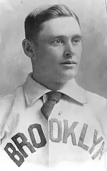 A man wearing a collared shirt with the words "BROOKLYN" at the front and a necktie.