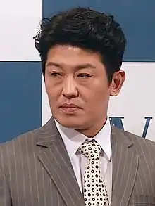 Heo standing in a grey suit and looking left