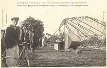 A postcard:On the right, an airship's gondoloa and keel lie on the ground on the side; on the left several people stand looking toward the camera.