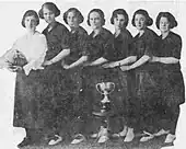 A line of seven women standing behind a large trophy