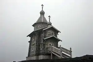 A small but detailed wooden structure built with a front staircase and topped with two onion domes.