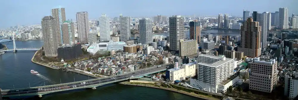 Upper portion of Tsukishima (island neighborhood), Chūō Ward, Tokyo, Japan. Tsukudajima, with its small houses, appears at the forefront. The Sumida River crosses in the foreground; the bridge on the bottom left is the Tsukuda Bridge (Tsukuda Ohashi), above that is the white Chou Bridge (Chuo Ohashi), and above that the blue Eitai Bridge (Eitai-bashi).