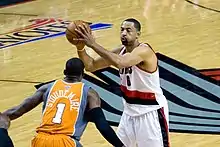 Black athlete holds a basketball while a defender with his back to the camera plays defense