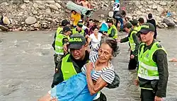 Venezuelan migrants crossing a river, aided by Colombian police