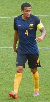 A man with dark hair in a green football jersey and green shorts.