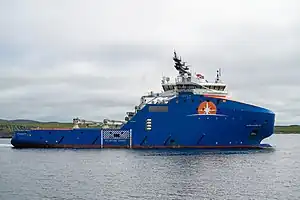 The arctic tug Horizon Arctic is shown facing to the right in this photograph. It is a large ship with a massive bow and reinforced hull designed for light icebreaking duties, painted royal blue to match the Horizon Maritime colors; the starburst logo is painted just beneath its white-painted bridge in the forward section of the hull. The rear half of the vessel has a much lower freeboard to accommodate surface operations.