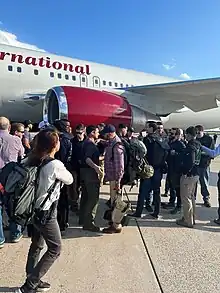 People with backpacks and sunglasses standing under a plane wing