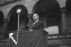 Man standing at an outdoor podium, speaking through a microphone