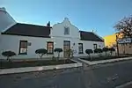 Thatched 5-bay Cape Dutch house with mock-chimney end gable, attached to No. 38. Wide holbol gable with semicircular pediment and blocked-up window. 3 × 3 double door with geometric fanlight, c 1850 (F & C), 2 × 2 sashes. Full-length hipped verandah on p Type of site: House Current use: House.