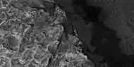 Layered features, as seen by HiRISE.  Light-toned materials often form on Mars with the aid of water. Gray material in image is probably dark, basalt sand.