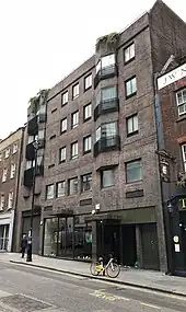 A five-storey brick building with a shop on the ground floor and flats above