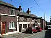 A row of three low cottages in sandstone with painted stone window surrounds