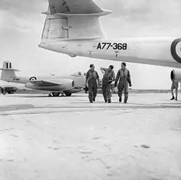 Three men in flying suits walking among twin-jet military aircraft