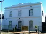 Double storey, 3-bay house with stepped-up parapet decorated with scrolls and two string courses with two rectangular and one round vent between. Corner quoins and moulded plaster surrounds to openings. Small 6 × 6 sashes to first floor. Large 6 × 6 sash Type of site: House Current use: House.