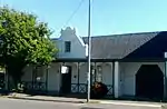 3-bay Cape Dutch house with iron roof and straight end gables. Front gable has 4 pilasters and winged cap and 3-pane casement. Verandah on plastered brick columns. 6 × 6 sashes; 3 × 3 double door with fanlight. On the right is a garage door with cut-off Type of site: House Current use: House. This excellent example of a gabled Worcester building, dating from c.1870, forms part of an unusual complex of adjoining buildings. The attached waenhuis still retains its original clipped doors, traditional to Worcester.