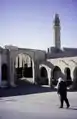 A round gate, the entrance to the carpet market. "Shop Berber". A satellite dish. A tower of a mosque, Tozeur, 1997.