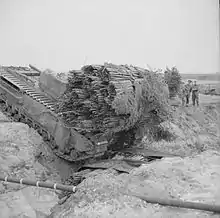 A Churchill AVRE, carrying a fascine, crosses a ditch using an already deployed fascine, (1943)