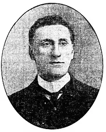 Grainy black and white photo of a man with short dark curly hair and a winged collar and tie