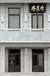 A 2008 closeup of the sign hanging outside the 2nd floor of the building. A North Korean soldier is seen guarding the first floor entrance.)