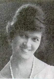 A young African-American woman, smiling, hair in a high updo, wearing beads.