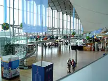 Inside a terminal, with a multi-story glass wall to the left; the open space is filled with signs, chairs, small store and amenities