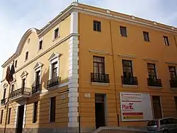 Honey coloured three storey building taken from a low camera angle against a pale blue sky