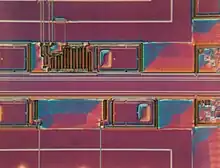 A problem in a silicon integrated circuit wafer. The pink and blue irregularly-shaped rectangles are areas of photoresist that should have been fully developed and rinsed away (purple), but there was a defect in processing. Seen under differential interference contrast microscopy.