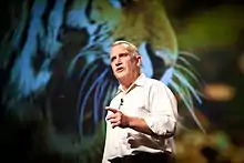  Man in beige shirt standing and talking, with finger pointed