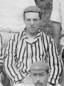 A black a white photograph of a man in a cap and stripped blazer sitting