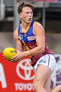 Male athlete in sleeveless guernsey holds football