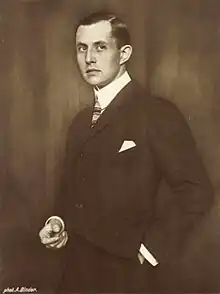 Man in suit with left hand in pocket facing left