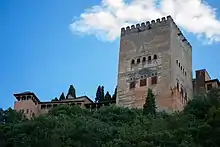 A Moorish style rectangular tower rising above trees and smaller buildings