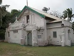 A picture of a small white church with spires, nestled next to palm trees and bushes.