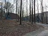 View of two small lodge buildings behind many thin trees.