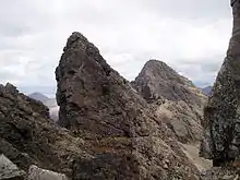 Rugged mountain scenery - several sharp prominences of bare grey rock stand out on a long ridge leading to more hills beyond.