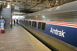 Stainless steel passenger rail cars with a thick blue stripe across the windows and two thinner red stripes above