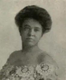 A woman with dark hair in a bouffant updo, wearing an off-the-shoulder lace dress