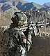 An Afghan National Army soldier in camouflage gear points a rifle over a dirt wall