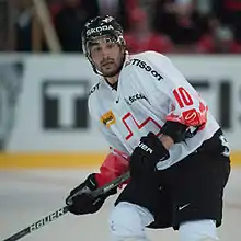 A Caucasian male ice hockey player shown from the knees up. He is wearing a red and white sweater with a black helmet.